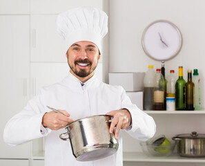 Smiling young male cook preparing delicious food in kitchen