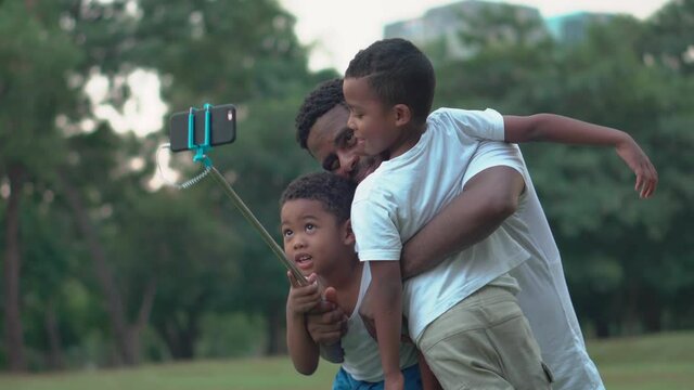 Father with little sons taking selfie picture with smartphone, Cheerful african american father and two sons playing in park