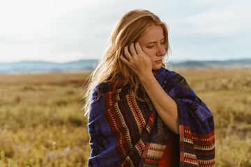 In the steppe against the hills a close-up of a girl straightening blond hair at the temple on her shoulders ethno cape. High quality photo