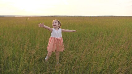 Naklejka na ściany i meble Kid catches butterfly in meadow in spring. Happy little girl runs across green field with outstretched arms. Child enjoys fresh air laughs and claps his hands. Cheerful child runs on green grass