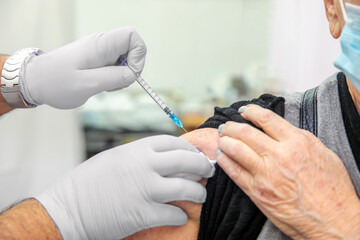Doctor vaccinating old patient in clinic with monouse syringe. Health worker with glove giving injection to senior man at hospital. Nurse holding syringe before make Covid-19 or coronavirus vaccine