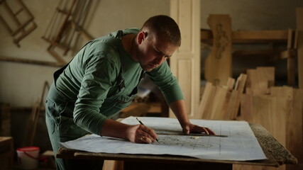 Focused man making drawings for wooden product indoors. Guy drawing ornament