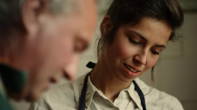 Senior man teaching woman in workshop. Lady learning pottery craft in studio