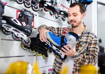 Positive smiling guy deciding on new roller-skates in sports store