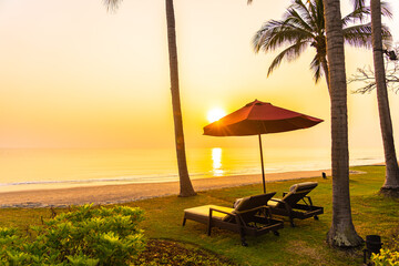 Umbrella and chair around outdoor swimming pool with sea beach ocean at sunset