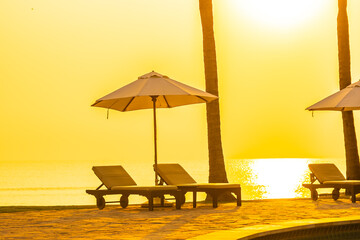 Umbrella and chair around outdoor swimming pool with sea beach ocean at sunset