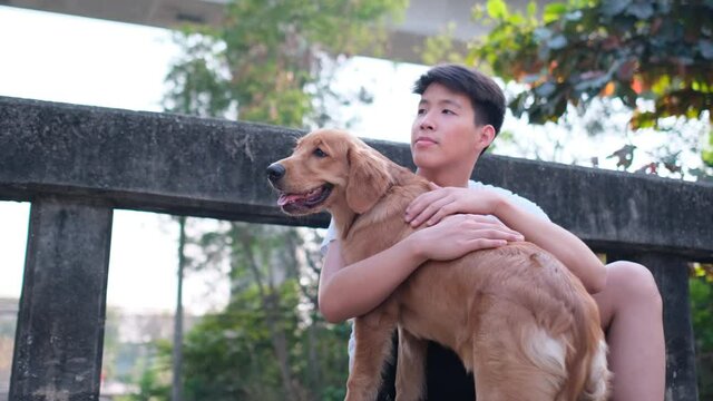 Asian young man hug his dog and sit on bridge and sideroad with happy emotion and evening light for relax time after work.