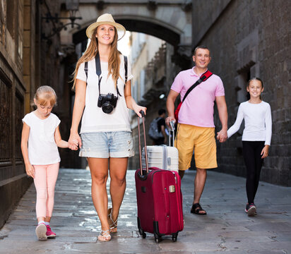 Family of four travelling together on city, walking with luggage