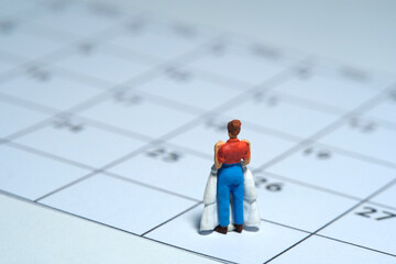 Woman miniature people stand above calendar while holding wedding dress, fitting day concept. Image photo
