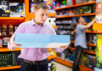 Interested adult man shopping in store of kids toys, holding carton with new plaything