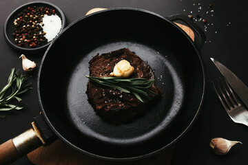 Ribeye steak on cast-iron pan, board with rosemary, garlic, knife, fork, butter