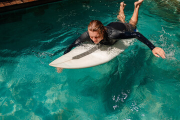 Young surfer paddling on surfboard in the swimming pool, training the surf technique