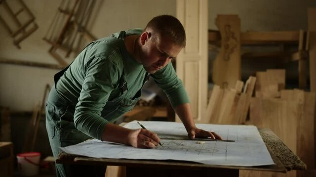 Focused man making drawings for wooden product indoors. Guy drawing ornament