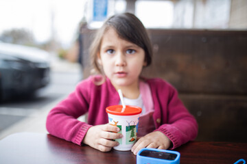 Cute little girl drinking from a cup with straw