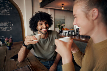 Cheerful young couple enjoying date while talking and laughing in modern cafe and drinking freshly brewed coffee