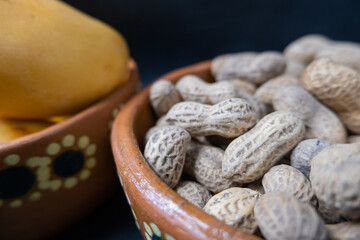Peanuts in a brown clay bowl with mangoes as background