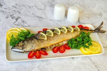 Oven baked mackerel on a white plate with lemon and cherry tomatoes