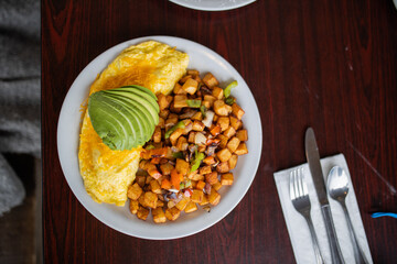 Omelette, roasted potatoes and avocado slices on a white plate