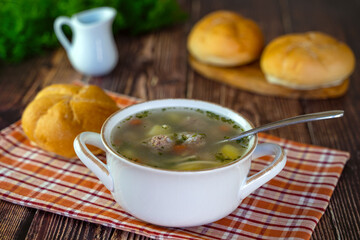 Hot soup with meatballs and vegetables in a wooden bowl on a wooden table. 