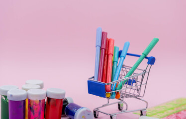 Bright stationery objects in mini supermarket cart on pink background. Back to school concept.