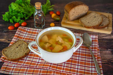 Traditional Russian fish soup (Ukha) with salmon, potatoes, onions and carrots in a bowl on a wooden table, near homemade black bread.