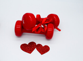 Two red dumbbells with a ribbon bow and two hearts on a white background. Soft focus. Concept of...