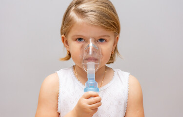 four-year-old girl with asthma and allergies makes inhalation in a mask with medicine through a...