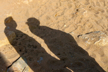 Silhouette of a pregnant couple standing on a sandy trail, the shadow of the pregnant woman castes across the sand.