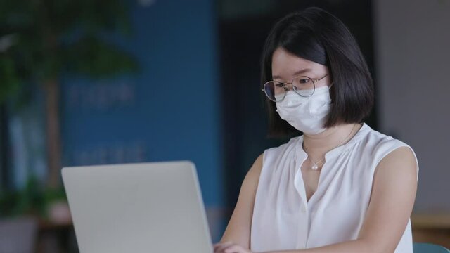 Asian Businesswoman Wear Face Mask And Social Distancing Sitting In Clean And Modern Office Without COVID-19. Meeting Working Online Via Laptop Using High Speed Internet Technology. Video Conference
