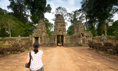Young woman walking in Angkor Bat towards a temple wearing a white t-shirt and a bag.