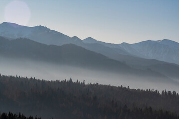 Multi layered mountainscape view. Tatra Mountains on a sunny December day. The fog is in the valleys between the ridges. Selective focus on the forest, blurred background.