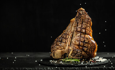 Grilled Premium Dry Aged T-bone Steak or porterhouse steak adding salt in a freeze motion on black...