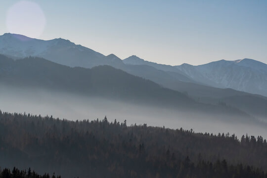 Multi layered mountainscape view. Tatra Mountains on a sunny December day. The fog is in the valleys between the ridges. Selective focus on the forest, blurred background. © juste.dcv