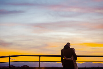 Back view of young couple in love watching sunset together during weekend