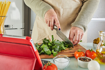 Woman cooking according the tutorial of online virtual master class, And looking on the digital recipe, using touchscreen tablet while cooking healthy meal on the kitchen at home