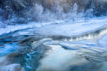 Mountain river and forest covered with ice, frost and snow in extremely cold weather.