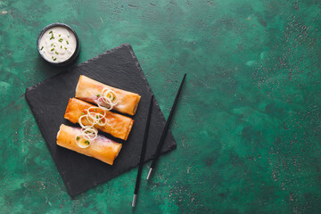 Slate plate with tasty spring rolls and sauce on color background