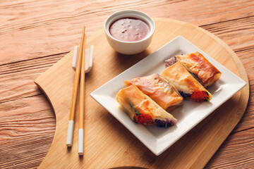Fototapeta na wymiar Plate with tasty fried spring rolls and sauce on wooden background