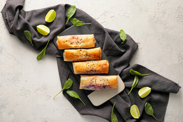 Plate with tasty fried spring rolls, lime and spinach on light background