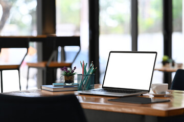 Computer laptop with blank screen, coffee cup ad office supplies on wooden office desk.