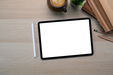 Above view of digital tablet with empty screen, stylus pen, coffee cup and notebook on wooden table.