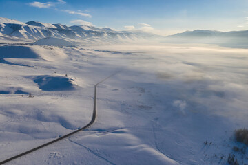 Aerial view of Chuya Highway running through winter covered with mist Kuray steppe. Altai Republic, Siberia, Russia..