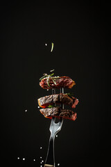 Naklejka na ściany i meble sliced steak medium rare, dry aged wagyu porterhouse beef steak with large fillet piece on a fork adding rosemary and sea salt in a freeze motion on black background. vertical image, American cuisine