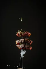 Foto op Canvas sliced steak medium rare, dry aged wagyu porterhouse beef steak with large fillet piece on a fork adding rosemary and sea salt in a freeze motion on black background. vertical image, American cuisine © Надія Коваль