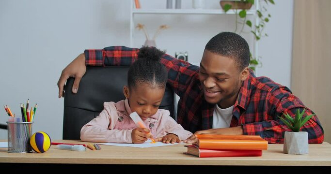 Afro american guy loving father helping little cute preschool daughter to draw picture do homework supports child gives five hands gesture of approval for teamwork excellent results, home teaching