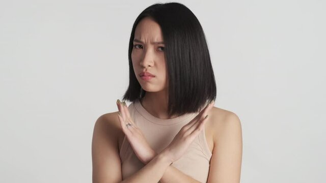 Serious Asian girl looking angry showing no gesture with crossed hands on camera over white background