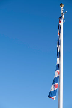 White mast with the flag of the province of Friesland. Blue with seven red seeblatts (or 'Pompebled') and four blue and three white diagonal stripes. Frisian flag at blue sky