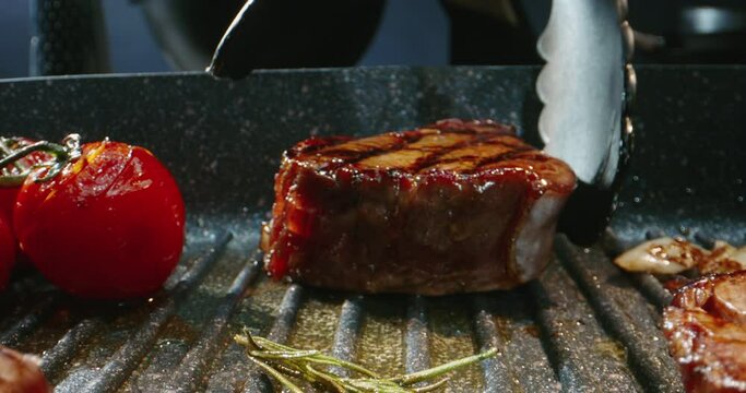 The chef flips a piece of grilling meat on grill pan