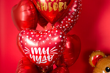 A large foil bear and a set of balloons in the form of hearts for Valentine's Day on a red background. Inscriptions in Russian balloons: "You are a miracle", "My love".