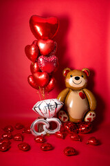 A large foil bear and a set of balloons in the form of hearts for Valentine's Day on a red background.